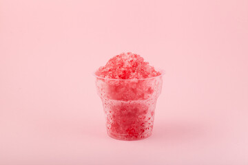 Fruit shaved ice in disposable plastic cup. Slushie - drink on pink background. Take away food....