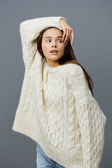 a beautiful, gentle, sophisticated woman with long hair stands in a stylish sweater on a gray studio background touching her head with her hand