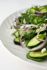 Light summer salad of cucumbers, onions and feta cheese in an oval white dish, close-up
