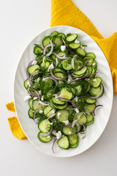 Light summer salad of cucumbers, onions and feta cheese in an oval white dish, top view
