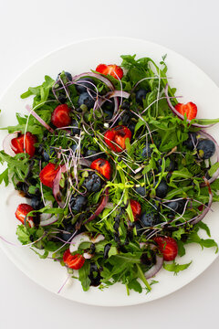 Light salad with arugula and berries, strawberries and blueberries, delicious healthy summer salad on a white background