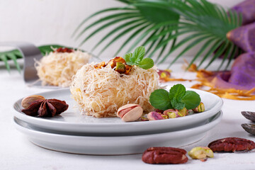 Kunafa dessert made of kataifi dough with pistachio and pecan nuts served on the plate. Egyptian...