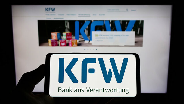 Stuttgart, Germany - 06-10-2022: Person holding mobile phone with logo of German bank Kreditanstalt fur Wiederaufbau (KfW) on screen in front of web page. Focus on phone display.