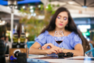 Young woman looks anxiously through a glass of wine in a street cafe, selective focus on the glass