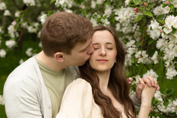 Fototapeta premium beautiful pregnant woman walks in a blooming garden. husband hugging and kisses pregnant wife
