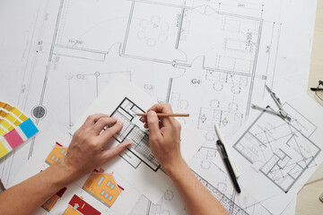 Hands of architect correcting apartment floor plan at his office desk, view from above