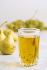 Juice of pears and grapes in a glass on a white wooden background