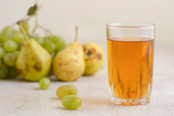 Juice of pears and grapes in a glass on a white wooden background