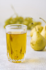 Juice of pears and grapes in a glass on a white wooden background