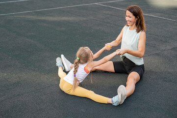 Mother and daughter go in for sports outdoors. Caucasian woman and little girl are engaged in fitness at the stadium.