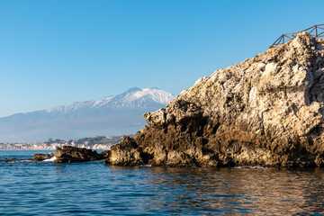 Fototapeta na wymiar Touristic boat tour with panoramic view from open sea on snow capped volcano Mount Etna and the Ionian Mediterranean coastline near Isola Bella in Taormina, Sicily, Italy, Europe, EU. Rock formations