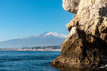 Touristic boat tour with panoramic view from open sea on snow capped volcano Mount Etna and the Ionian Mediterranean coastline near Isola Bella in Taormina, Sicily, Italy, Europe, EU. Rock formations