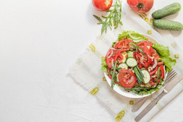 A white plate with fresh vegetables saladon a white background. Salad with cucumber, tomato, arugula, onion, lettuce. Copy space. Top view.