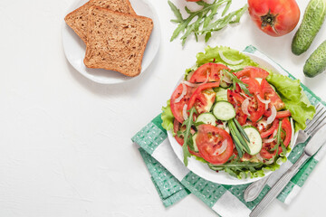 Fresh vegetable salad with cucumber, tomato, arugula, lettuce, onion and wholegrain bread on a white backgound. Copy space. Top iew.