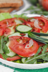 A white plate with fresh summer vegetable salad close up on a dinner table.