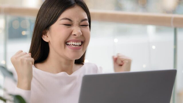Close up happy excited Asian girl winner with laptop celebrate triumph good news betting with online app. Successful lucky woman looking screen wins has new job offer shouts screams makes yes gesture