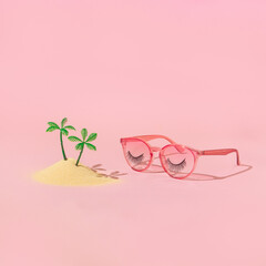 Summer holiday creative  layout with plam tree figurines in sand and pink eyeglasses with false eyelashes on pastel pink background. 70s, 80s or 90s retro aesthetic fashion surreal concept. 
