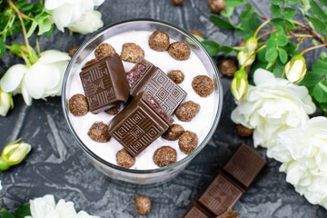 Multi-layer cottage cheese dessert with yogurt, chocolate balls and chocolate slices with filling, bushy white roses on a black (dark) background. Close-up. Romantic breakfast. Top view.
