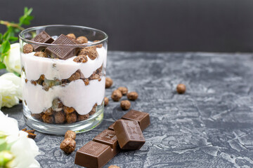 Cottage cheese-yogurt multi-layer dessert with dark chocolate slices and corn balls, white bush roses on a black (dark) background. Recipe, ingredients. Space for the text.