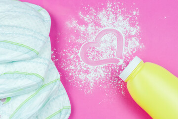 Scattered baby powder in a yellow bottle with a heart pattern on the powder and diapers on a bright pink background. Children's concept. Love for the baby.