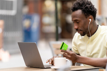 Young man shopping online with a credit card and a personal computer in the street