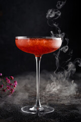 Strawberry daiquiri cocktail in a beautiful glass with crushed ice and smoke on a dark background. Tropical alcoholic drink with rum, close up