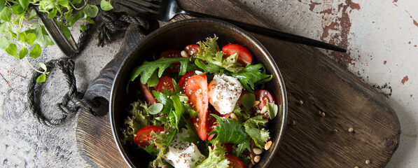 bowl with salad with arugula, tomatoes and cream cheese on the table