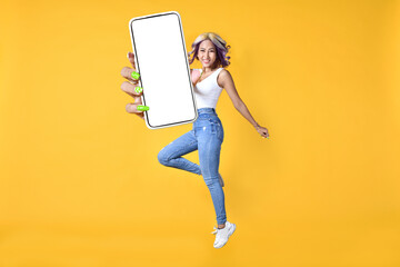Excited young Asian woman holding smartphone, showing blank screen, jumping up over yellow studio background. Attractive female recommending new mobile application, creative collage with mockup
