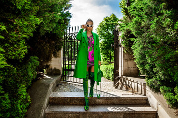 Fototapeta na wymiar Spring, summer fashion. High fashion model. Glamour, stylish elegant woman. Female model in colorful dress and Trendy green coat in the city. Outdoor shoot. Casual, urban style. Vogue.