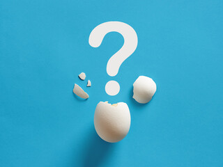 Cracked white chicken egg shell with question mark symbol. Surprise, mystery, uncertainty or baby gender prediction