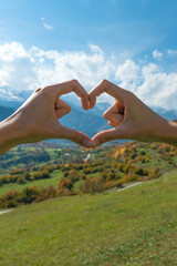 Close-up of a young woman's hands creating the shape of a love heart with her hands against the background of autumn mountains on a sunny day. Concept of travel, the passion for travel.