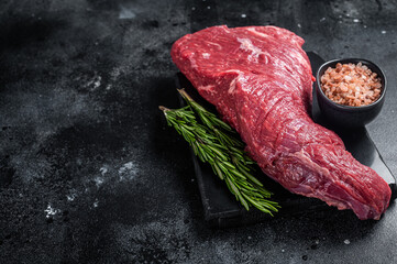 Raw American Tri Tip beef steak on marble board. Black background. Top view. Copy space