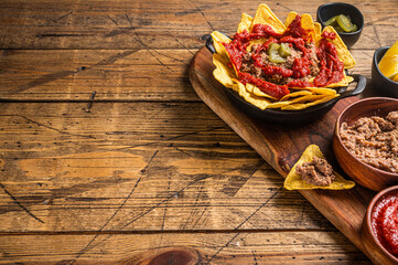 Traditional mexican refried beans with nachos, jalapeno and tomato sauce. Wooden background. Top...