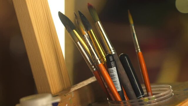 Painting tools, brushes and bottles with paints are on the wooden rack, in beautiful studio filled with soft morning sunlight, atmosphere of magic and art, Zoom out, Slow motion. FullHD footage