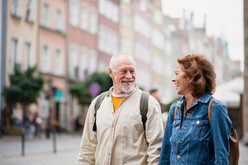 Portrait of happy senior couple tourists using smartphone outdoors in historic town