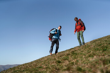 Paragliders walking up hill to paragliding starting point, on sunny morning in mountains.
