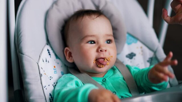 Little toddler nutrition in baby chair. Mother shoves the full spoon into a kid's mouth. Close up.