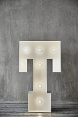 An unusual lamp in the form of the letter t stands on a gray floor.