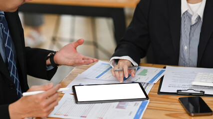 Cropped shot business colleagues using digital tablet and analyzing marketing research reports together at office desk