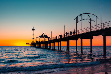 Iconic Brighton jetty with people silhouettes at sunset viewed from the beach, South Australia