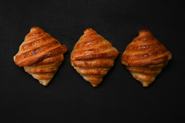 Warm fresh buttery croissants on black wooden table. Breakfast, bread bakery products cafe concept