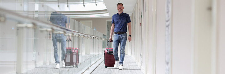Fototapeta premium Young man with suitcase walking down hotel corridor