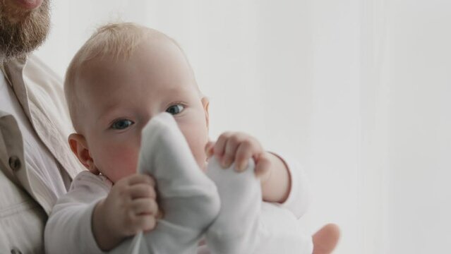 Close-up of little Caucasian cute funny infant newborn daughter son with unrecognizable father. Child playful kid holding himself by legs baby socks looking at camera playing, childhood game at home