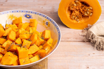 Diced pumpkin pieces in a bowl, with spices and olive oil