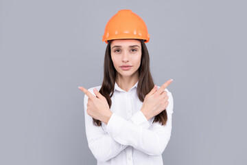 Young woman wearing hardhat pointing gesture. Architect woman wearing helmet over gray background.