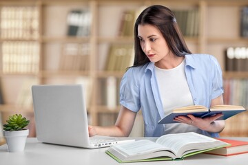 Young student girl sit at table, studying alone in library, looks pensive and thoughtful search solution, prepare for exam, makes task feels confused or puzzled