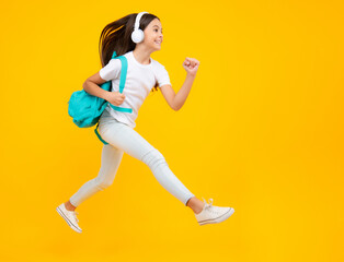 Schoolgirl, teenage student girl in headphones on yellow isolated studio background. School and music education concept. Back to school. Excited teenager, jump and run, jumping child.