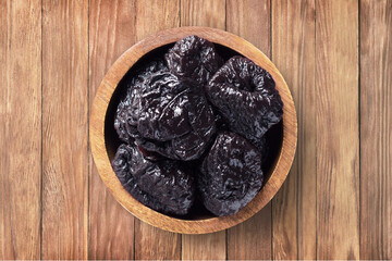 dried plums, prunes in bowl on wooden table background, top view. organic vegetarian food.
