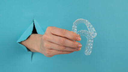 A female hand sticking out of a hole from a blue background holds removable night retainers. 