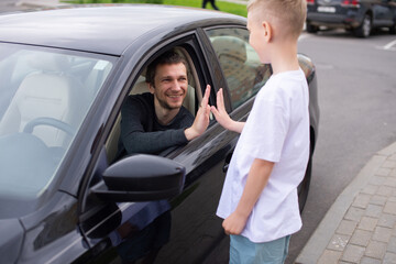 A cute child accompanies a happy father to work. Dad is sitting in the car. Give five